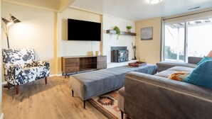 A living room with a sofa, a chair, a TV, a fireplace, and a window. - Spacious 6 BR Extended Stay (North Salt Lake)