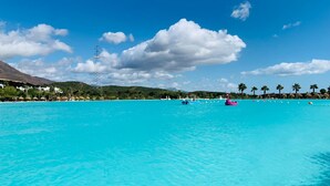 Une grande piscine d’un bleu turquoise éclatant, avec des bateaux et des flamants roses, entourée de palmiers et de bâtiments.