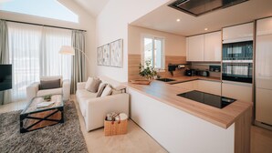 Une cuisine moderne avec un îlot central, un coin repas avec un canapé et un salon équipé d’un téléviseur.