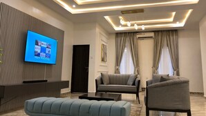 Ein modernes Wohnzimmer mit einem wandmontierten Flachbildfernseher, einer Couch, zwei Sesseln, einem Couchtisch und einer Bank.