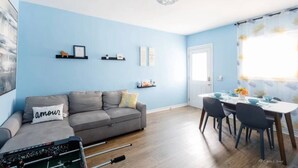 Ein modernes Wohnzimmer mit einer grauen Couch, einem Esstisch mit Stühlen und einem Kronleuchter.
