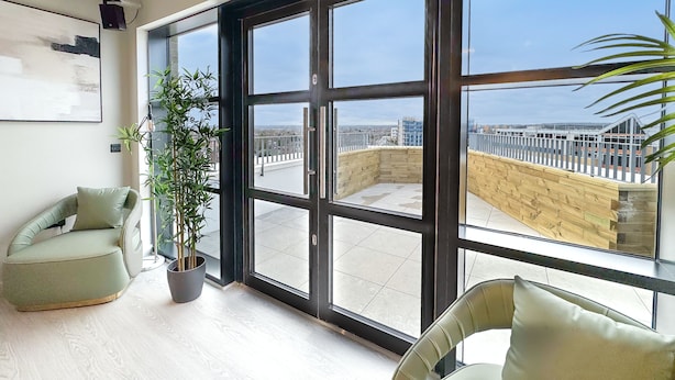 A spacious balcony with large windows, a potted plant, and a modern chair.