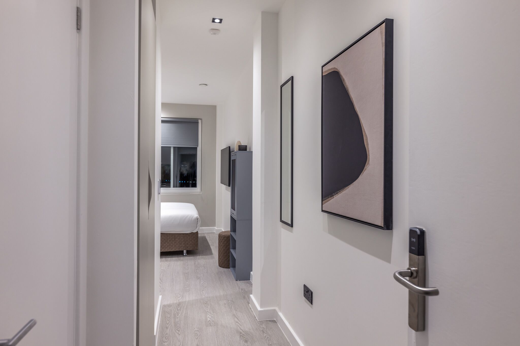 A hallway with a bed, a television, and a door with a handle.