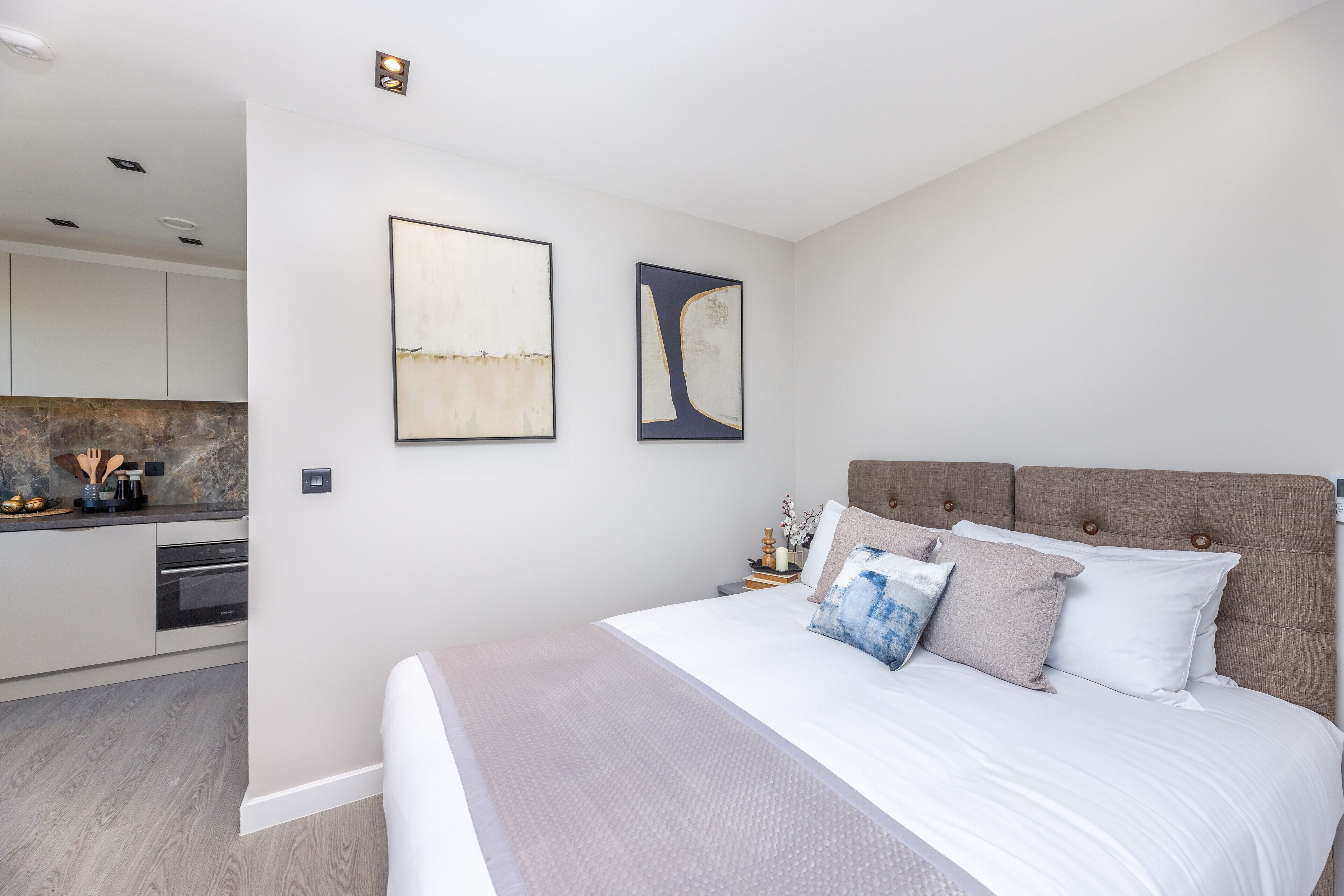 Een moderne slaapkamer met een groot bed, een hoofdeinde en twee abstracte schilderijen aan de muur.