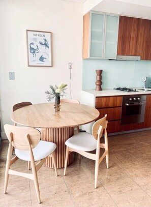 Une cuisine moderne avec des meubles en bois, une table de salle à manger ronde entourée de chaises et une œuvre d’art encadrée accrochée au mur.