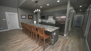 A modern kitchen with a central island, wooden chairs, and stainless steel appliances. -  Nocona Lakefront with 40 private acres, beds for 8, newly constructed in 2024! (Nocona)