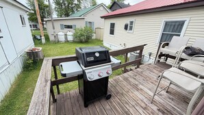 Takapihalla on Weber Spirit -grilli, puinen terassi ja valkoinen talo, jonka katto on punainen.