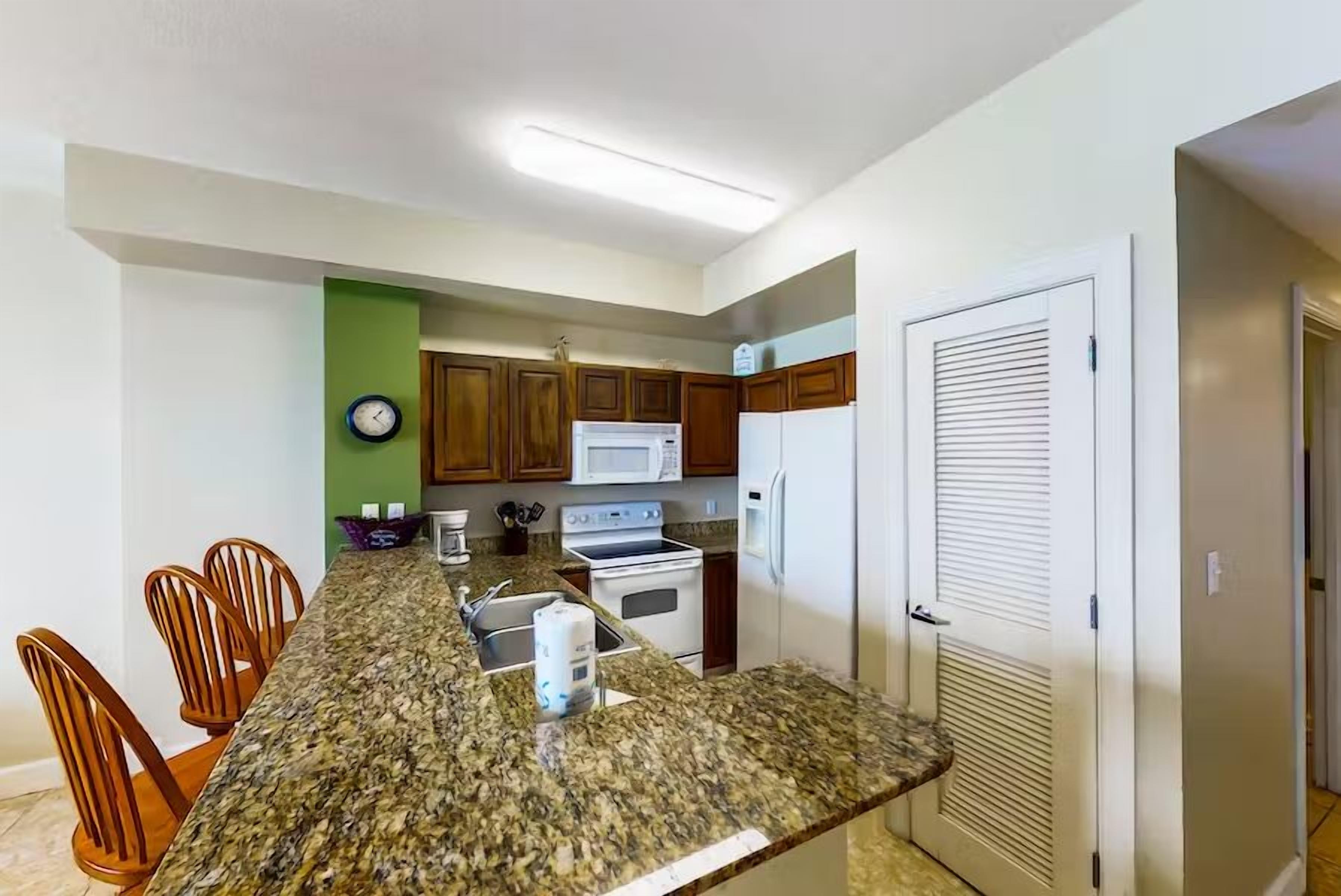 Una cocina con encimeras de granito, gabinetes de madera, microondas, estufa y refrigerador.