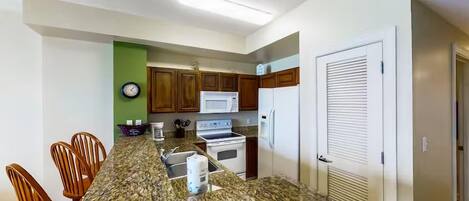 Una cocina con encimeras de granito, gabinetes de madera, microondas, estufa y refrigerador.