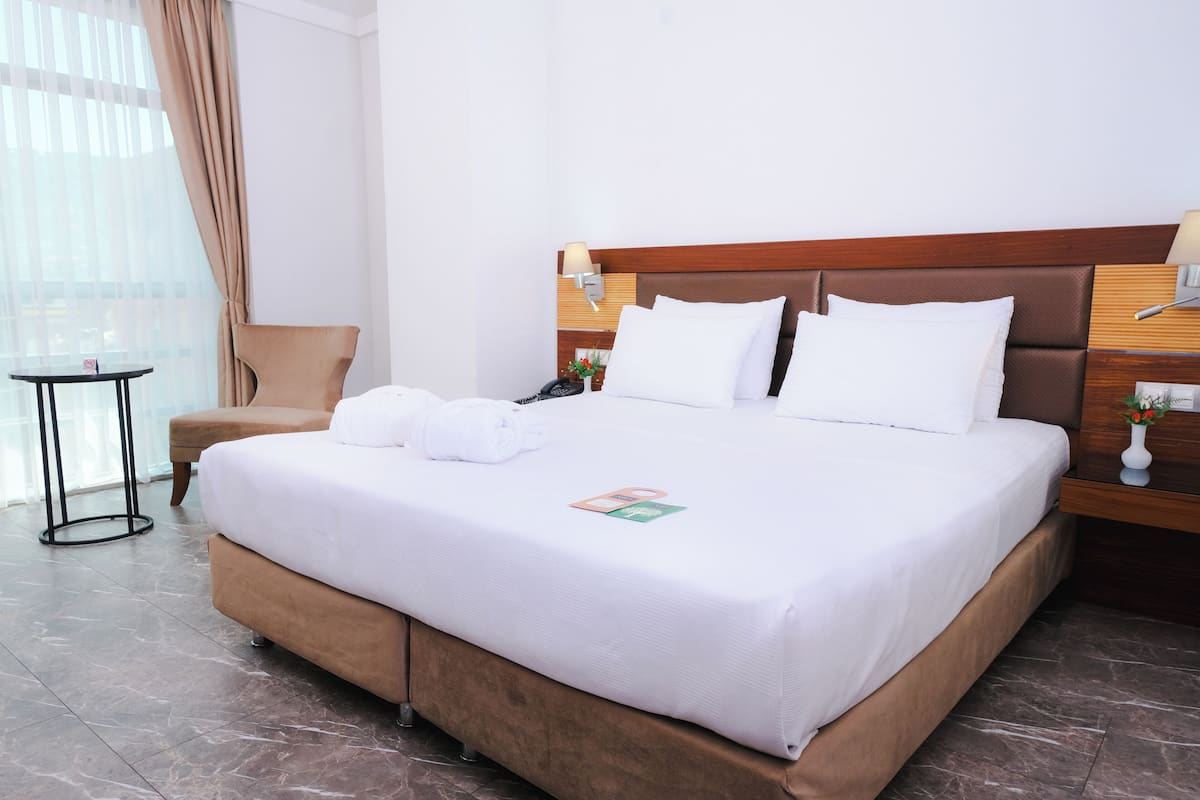 Una habitación de hotel con una cama grande, una silla, una mesita de noche, una lámpara y una pequeña mesa.