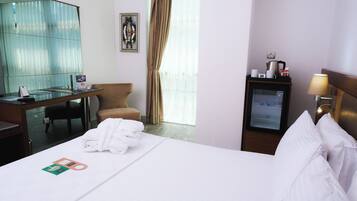 A hotel room with a bed, a desk, a chair, a minibar, and a window with curtains.