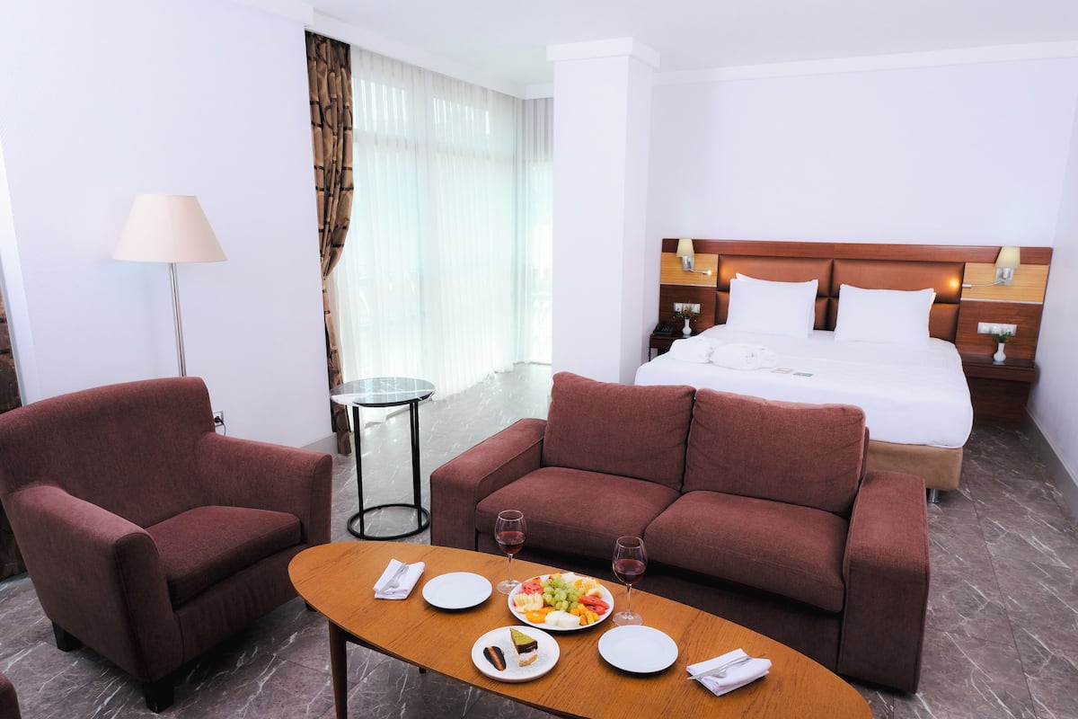 Una habitación de hotel con una cama, dos sofás, una mesita con platos y vasos, y una lámpara.