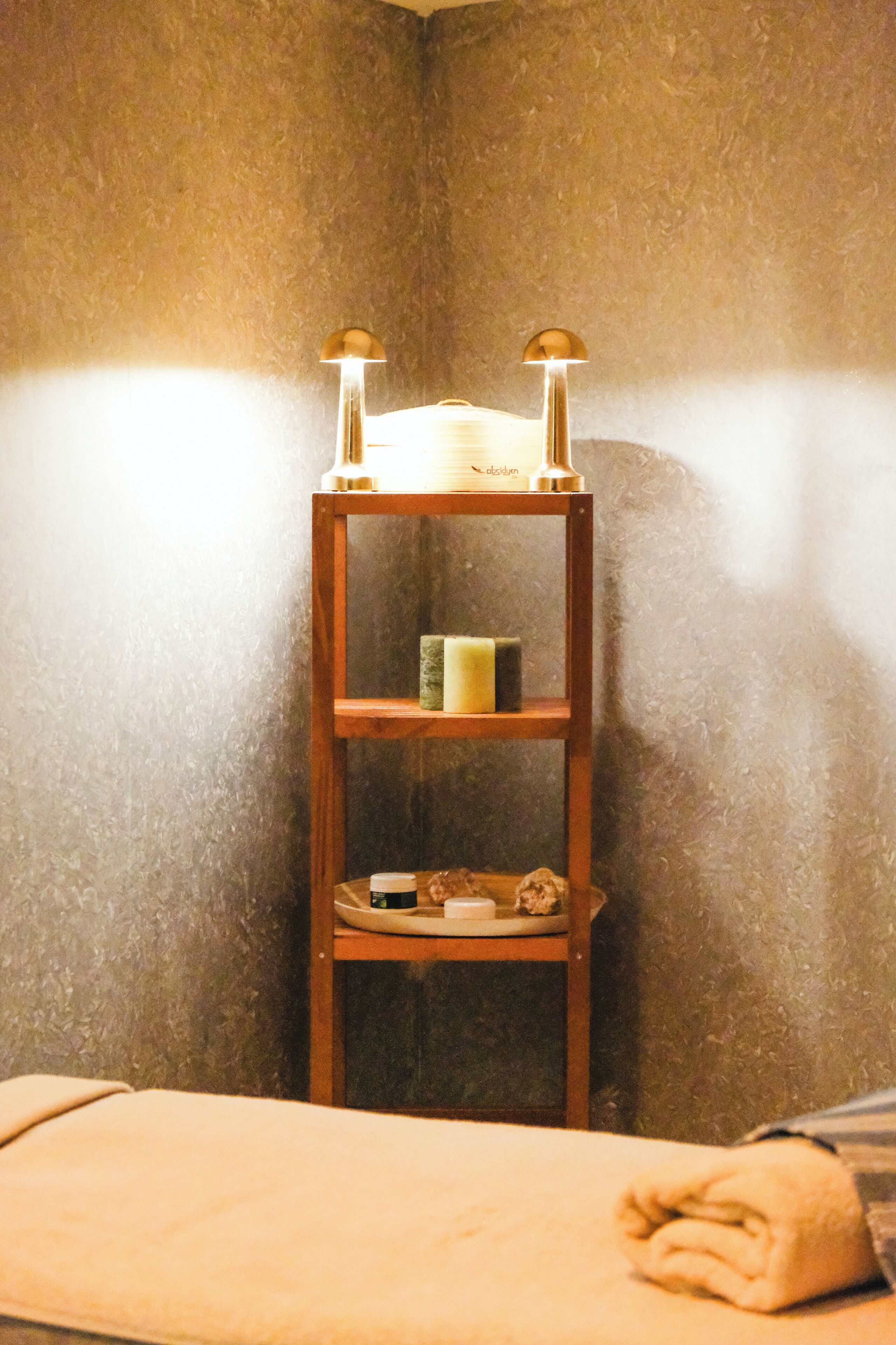 Un coin de pièce avec une étagère en bois sur laquelle se trouvent une bougie, une petite boîte et une assiette avec une tasse.