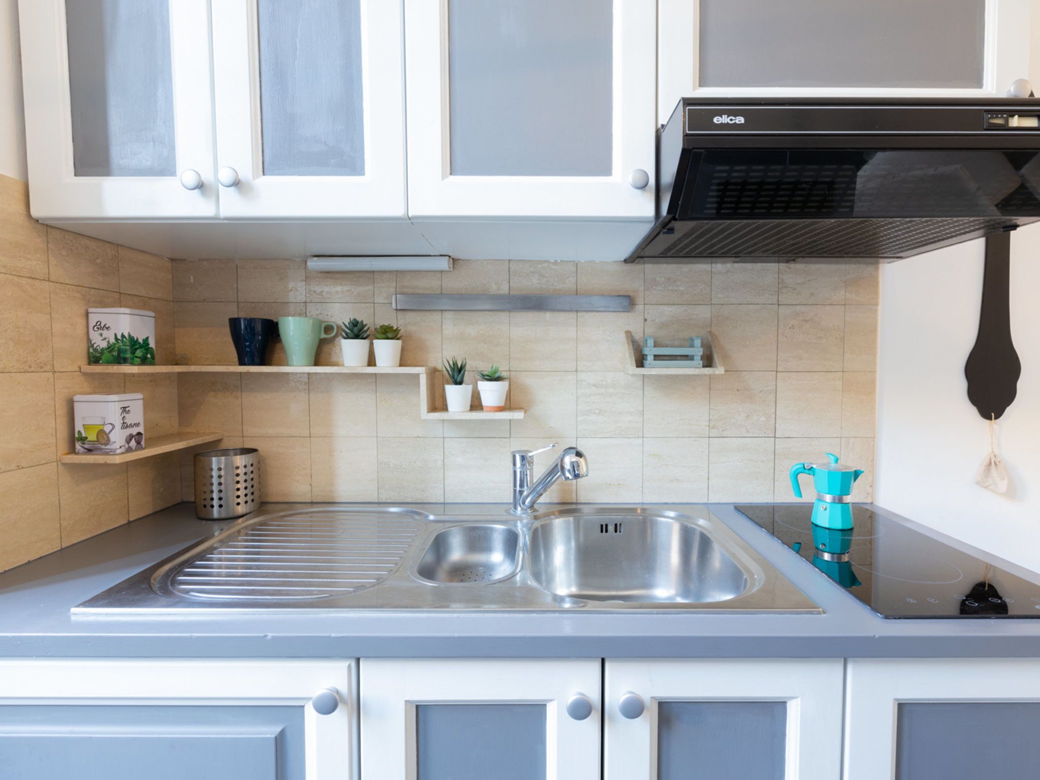 A modern kitchen with white cabinets, a stainless steel sink, and a black range hood.