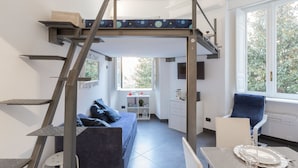 Un dormitorio estilo loft moderno con cama alta, un comedor y una cocina al fondo.