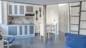 Una cocina moderna con armarios blancos, un comedor con mesa y sillas, y un sofá azul en la sala.