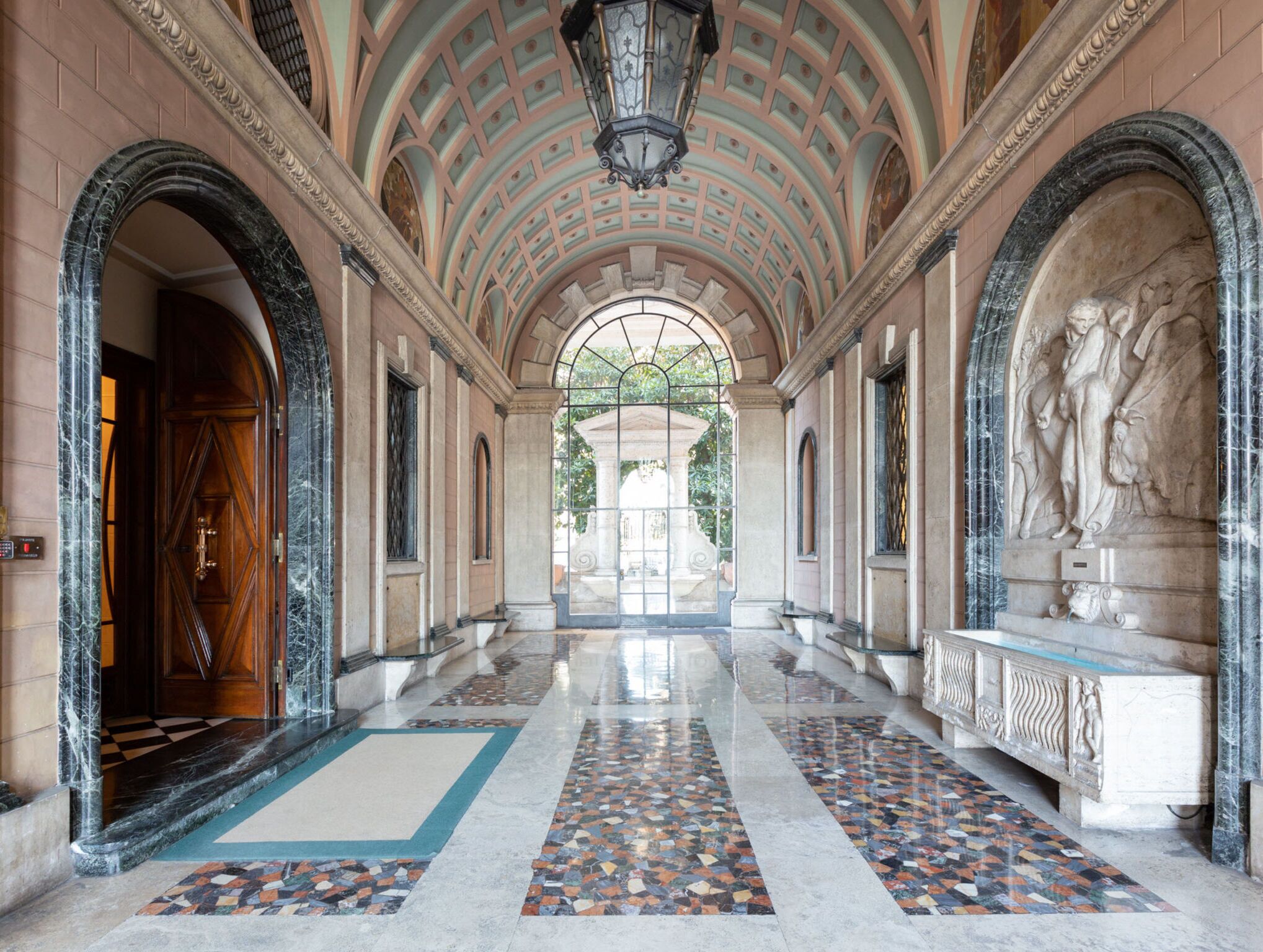 A grand hallway with a high ceiling, marble flooring, and classical statues.