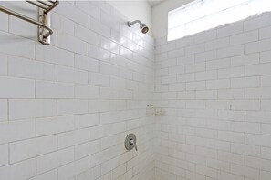 Ein Badezimmer mit weiß gefliesten Wänden, einer Duschbrause und einem Wasserhahn.