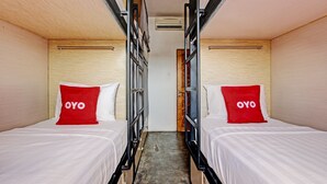 Un pasillo estrecho con dos camas a cada lado, cada una con un almohadón rojo etiquetado 'OYO'.