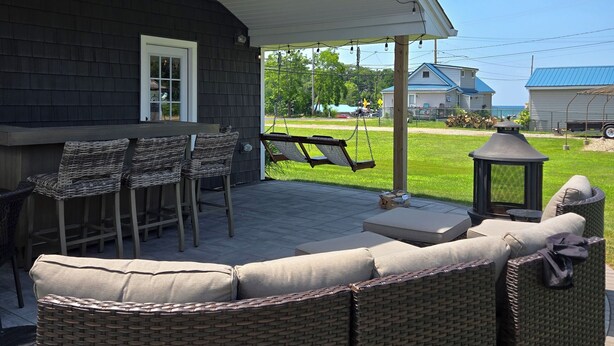 Une terrasse couverte, aménagée avec des meubles en osier, une balançoire et une lanterne.