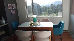 Uma sala de jantar com uma mesa, cadeiras e vista para uma paisagem montanhosa através de uma janela.