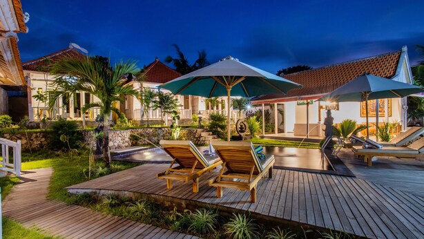 A wooden deck with lounge chairs and umbrellas, a swimming pool, and a stone wall. - Blue Sky Villa Ceningan by ABM  (Ceningan Island)