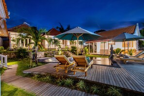 A wooden deck with lounge chairs and umbrellas, a swimming pool, and a stone wall. - Blue Sky Villa Ceningan by ABM  (Ceningan Island)