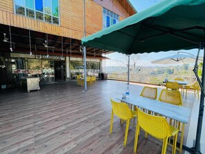 An outdoor patio with yellow chairs and tables, a covered area, and a view of the surrounding landscape. - Paradise Woodland Resort Chintpurni (Dera Gopipur)