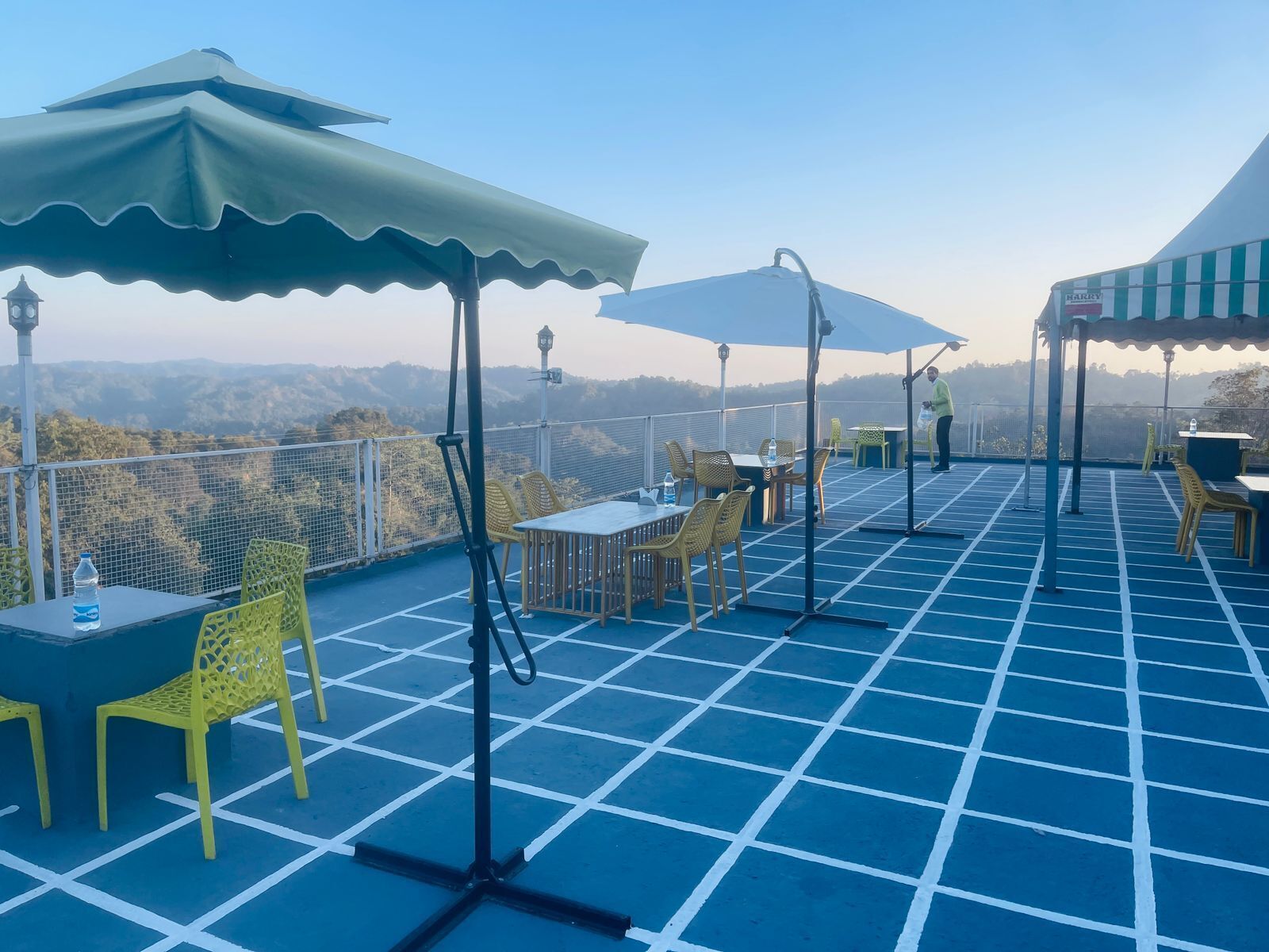 Une terrasse sur le toit, aménagée avec des tables, des chaises et des parasols, d’où l’on peut admirer un paysage montagneux.