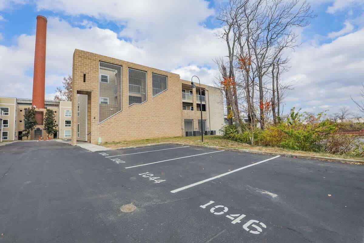 Een parkeerplaats met aangegeven parkeerplaatsen 1044 en 1046, een bakstenen gebouw met grote ramen en een hoge schoorsteen.