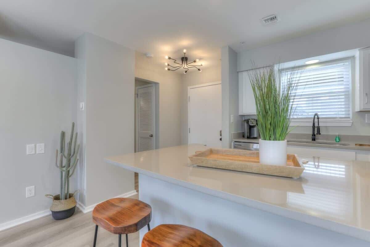 A modern kitchen with a central island, bar stools, a hanging light fixture, and a potted plant.
