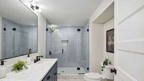 Een moderne badkamer met een douchecabine van glas, een wit toilet en een marmeren wastafelblad.