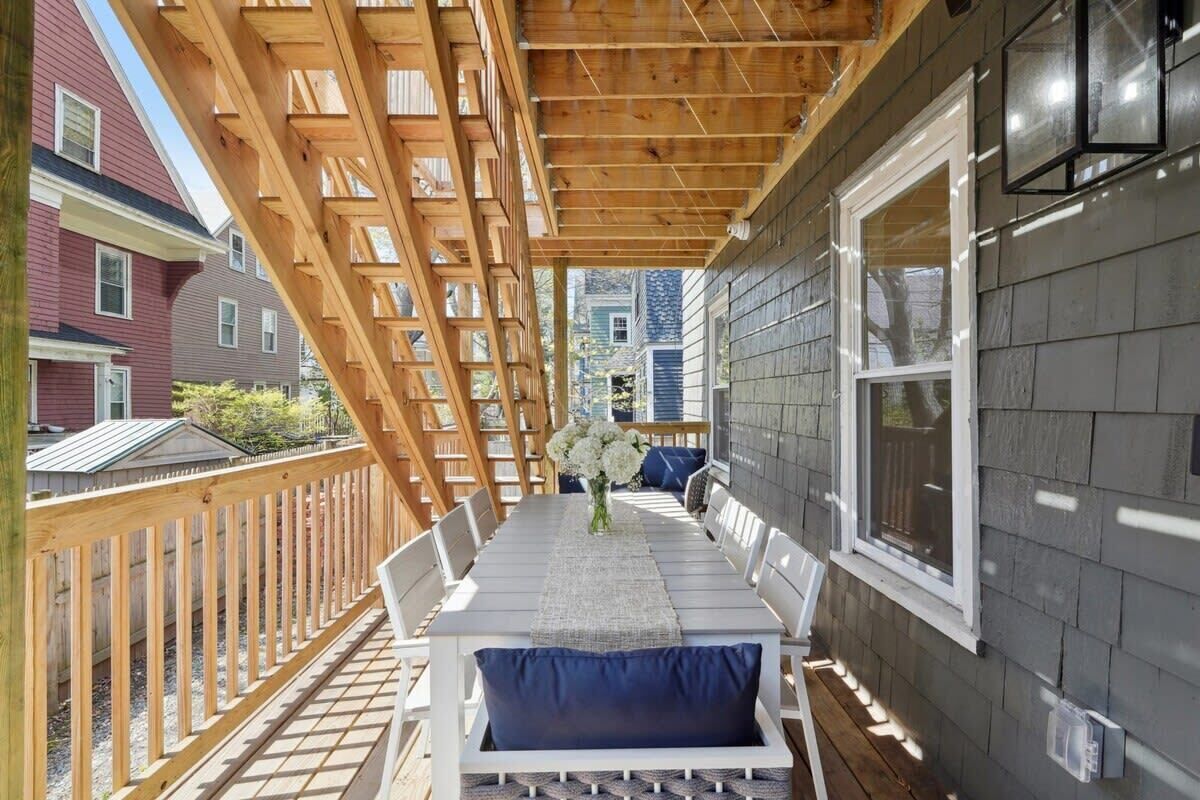 A covered outdoor patio with a wooden deck, white furniture, and a view of neighboring houses.