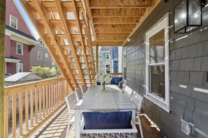 A covered outdoor patio with a wooden deck, white furniture, and a view of neighboring houses. - 6BR Classic Boston Home | Near Savin Hill T (Boston)