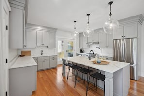 A modern kitchen with white cabinetry, a large island with bar stools, stainless steel appliances, and pendant lighting. - 6BR Classic Boston Home | Near Savin Hill T (Boston)