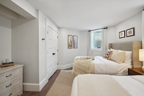 A bedroom with a bed, a nightstand, a dresser, and a window with curtains.