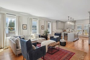 A spacious living area with a sofa, chairs, and a rug. There is a kitchen with cabinets and a refrigerator. - 6BR Classic Boston Home | Near Savin Hill T (Boston)