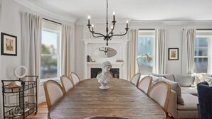 A dining room with a wooden table, chairs, a chandelier, and a fireplace.
