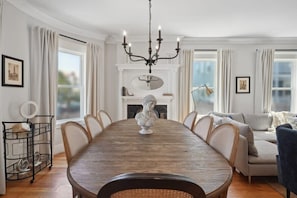 A dining room with a wooden table, chairs, a chandelier, and a fireplace.