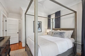 A four-poster bed with a wooden frame, white bedding, and a grey furry throw pillow. A bedside table with a lamp is visible to the right. - 6BR Classic Boston Home | Near Savin Hill T (Boston)