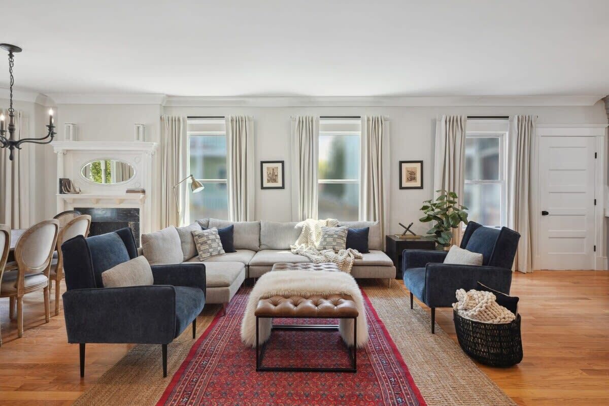 A living room with a sectional sofa, a tufted ottoman, a chandelier, and a fireplace.