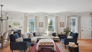 A living room with a sectional sofa, a tufted ottoman, a chandelier, and a fireplace.