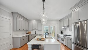 A modern kitchen with white cabinetry, a central island, stainless steel appliances, and a hanging light fixture.