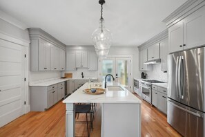 A modern kitchen with white cabinetry, a central island, stainless steel appliances, and a hanging light fixture.