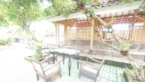 An outdoor patio with a table and chairs, surrounded by stone steps and greenery. - Hotel O Kencana Homestay Syariah Near Masjid AL-BAROKAH Kanyuran (Mojokerto)