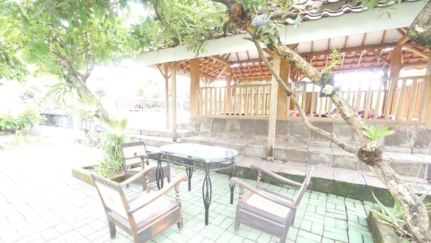 An outdoor patio with a table and chairs, surrounded by stone steps and greenery. - Hotel O Kencana Homestay Syariah Near Masjid AL-BAROKAH Kanyuran (Mojokerto)