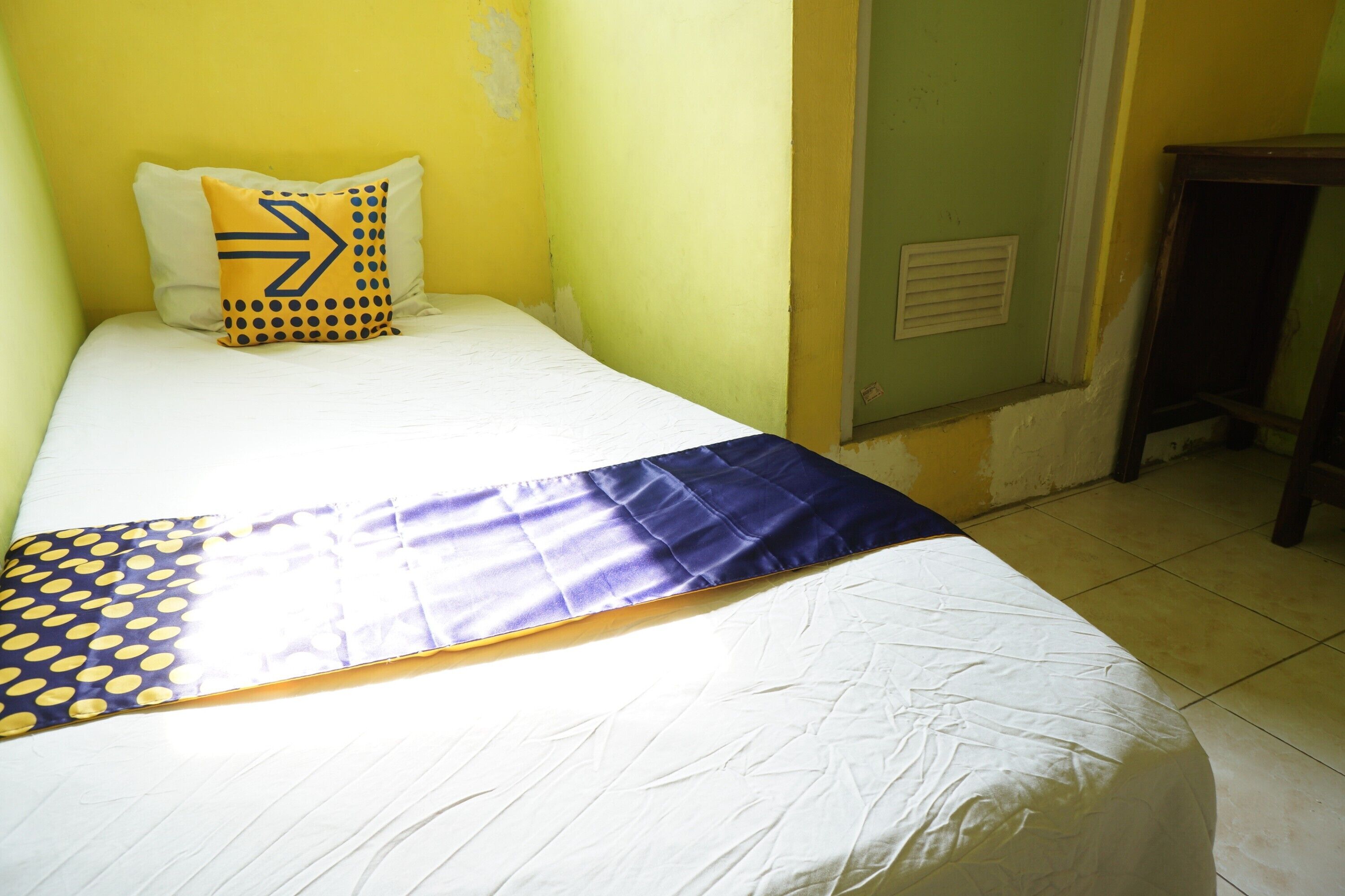 Una cama con colchón blanco, manta azul y amarilla, y almohada con estampado geométrico.