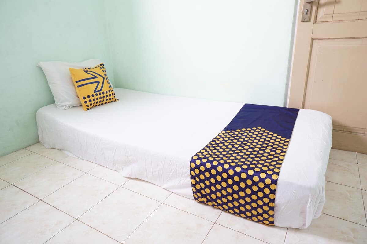 A single bed with a white mattress, a blue and yellow polka dot blanket, and a white pillow with a black arrow design.
