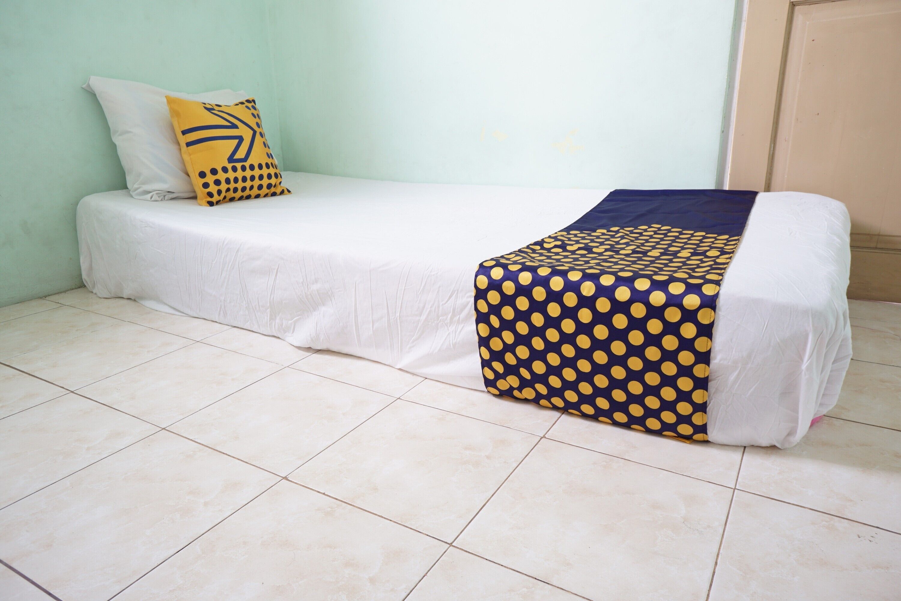 A single bed with a white mattress and a blue and yellow polka dot blanket.