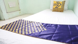 A bed with a white mattress, a blue and yellow polka dot blanket, and a pillow with a yellow arrow design. - SPOT ON 93611 Kost Pak Suyatno Syariah 2 (Ponorogo)
